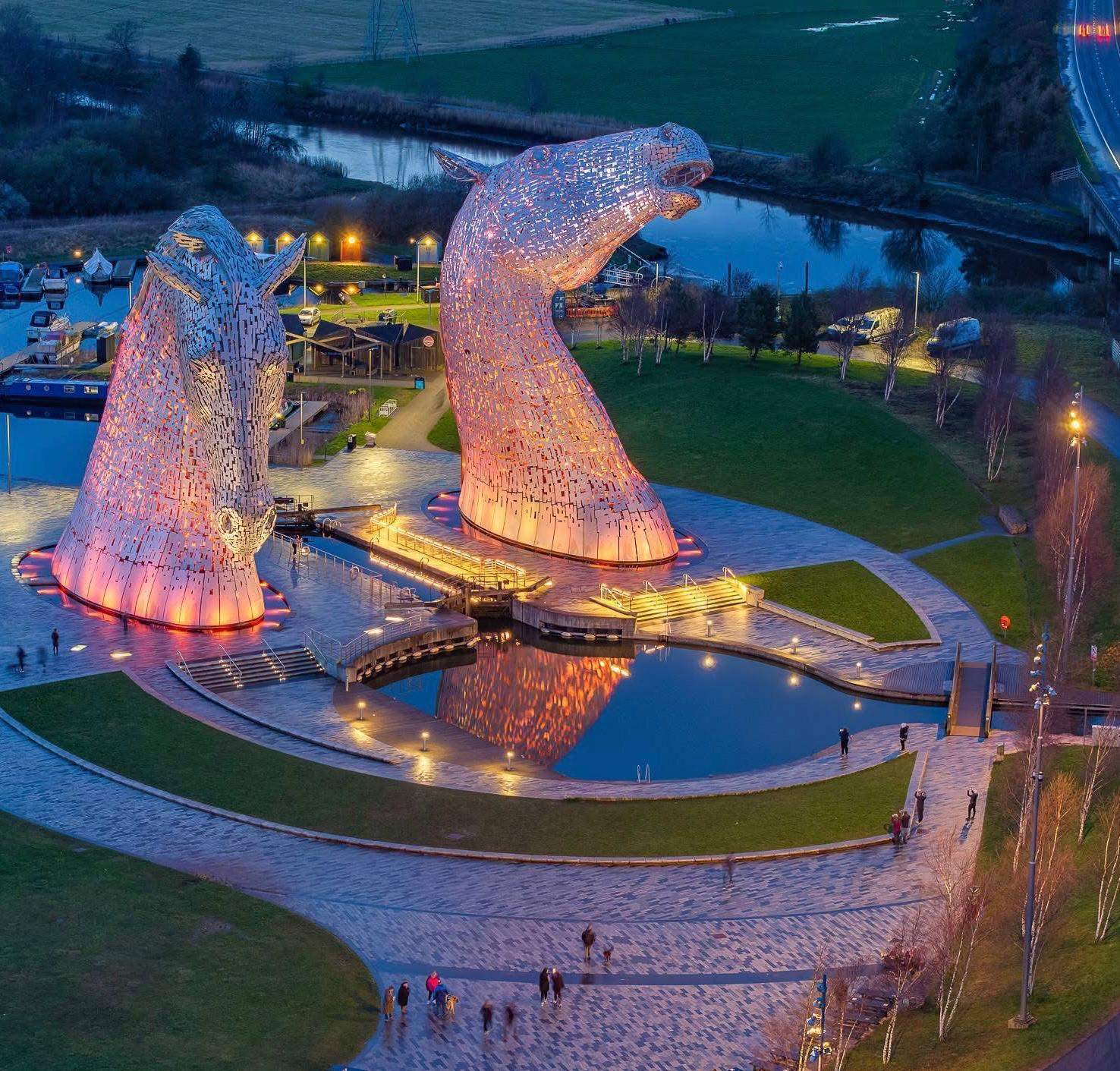 The Kelpies illuminated at dusk with reflecting pool